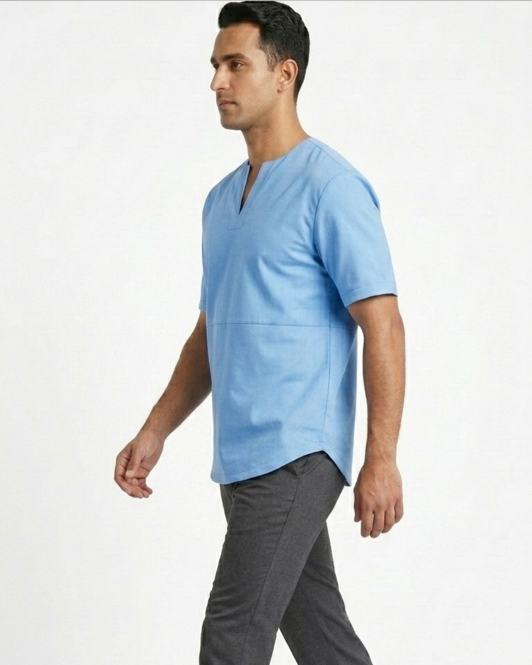 A man wearing a light blue V-neck leather tee shirt and dark gray trousers, shown in profile against a plain white studio background.