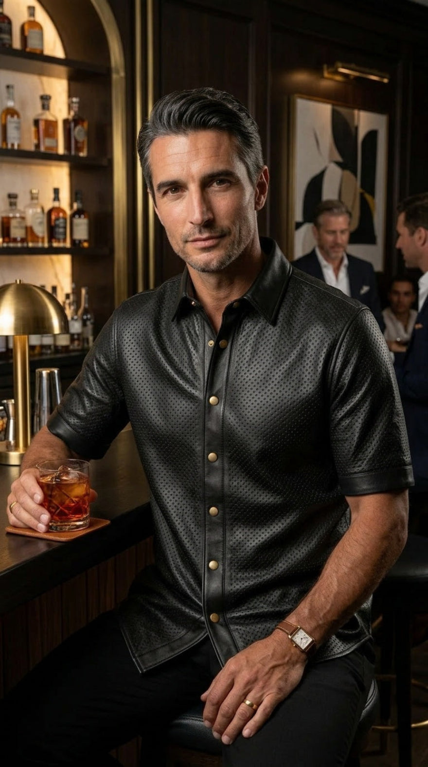 Man, wearing our Mens Black Perforated Leather Shirt | Short Sleeve Nappa Button Up, in a bar setting holding a glass of whiskey