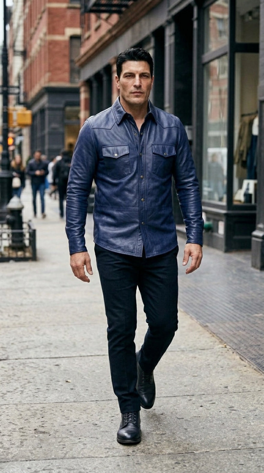 A man walking on a city sidewalk wearing our blue leather button-down shirt, black pants, and black boots.