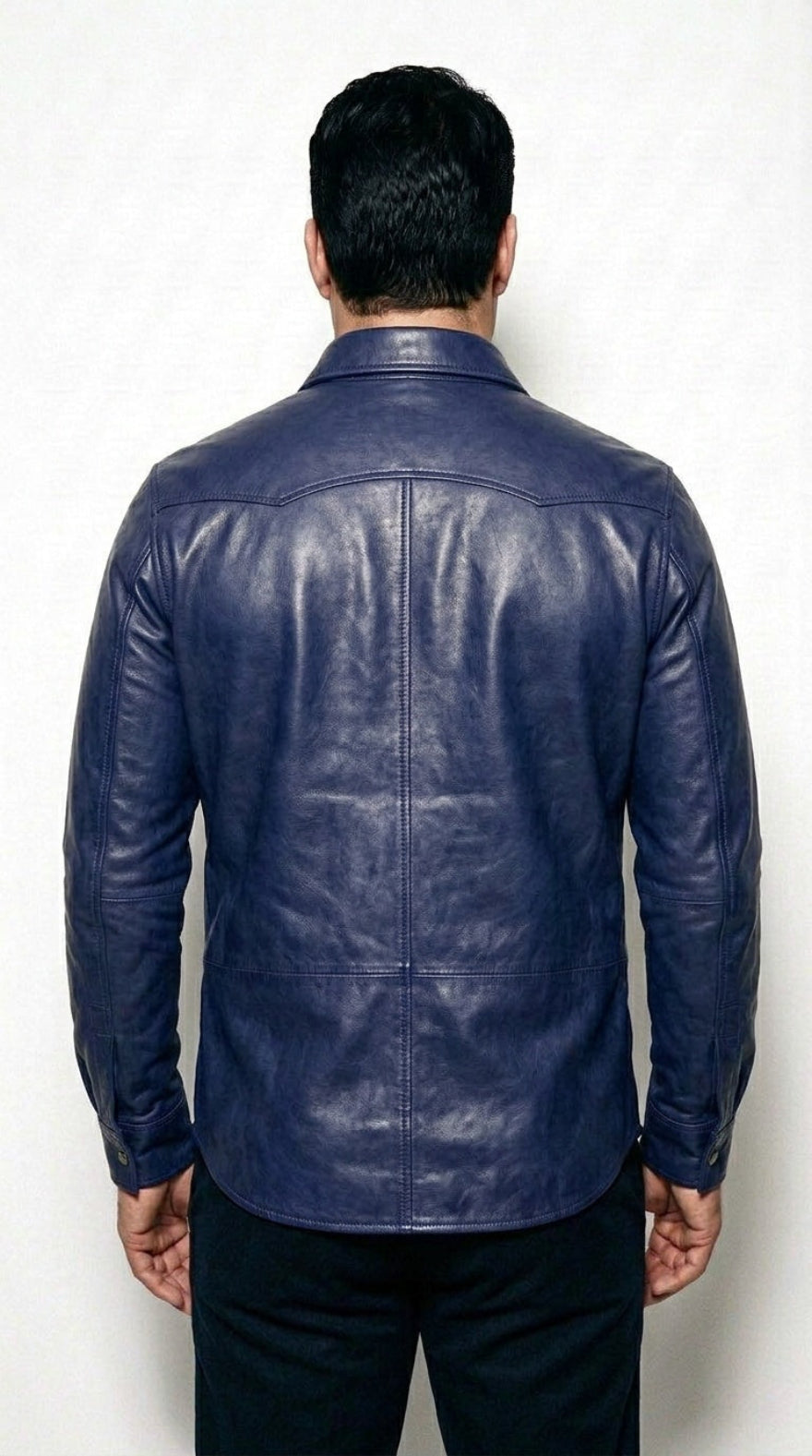 A man viewed from the back wearing our blue leather shirt and dark pants, standing against a light gray textured background.