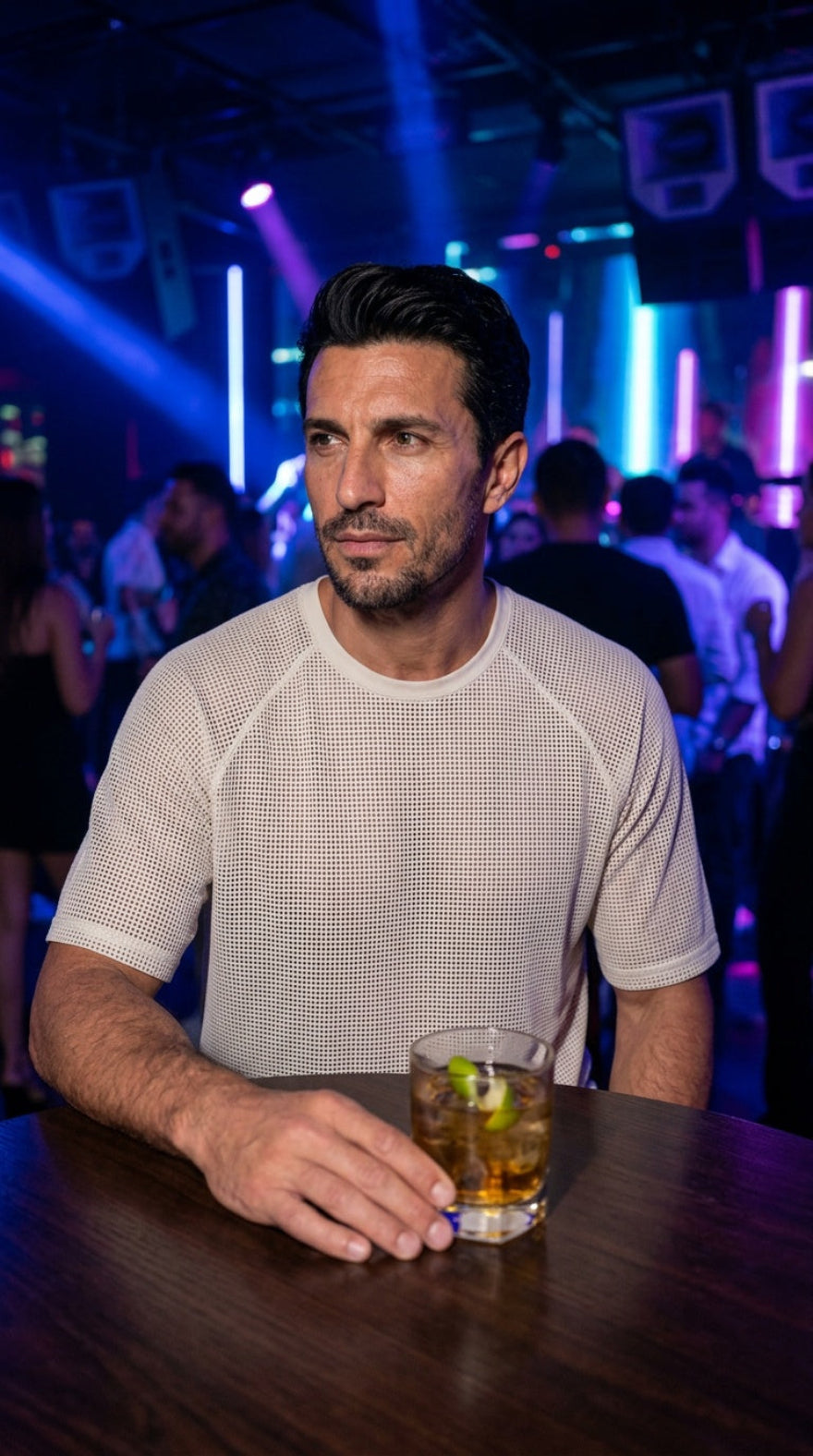 Picture of a model wearing our Mens White Perforated Leather Tee Shirt, sitting at a table in a club. 