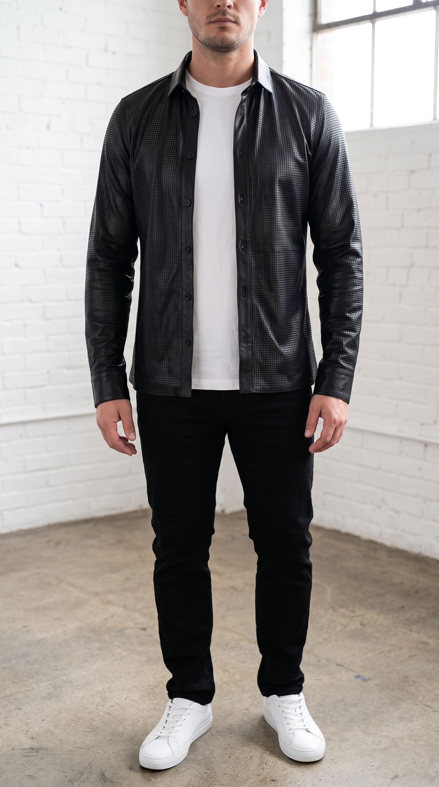 Model wearing a black perforated Nappa leather shirt unbuttoned over a white t-shirt in a bright modern loft.