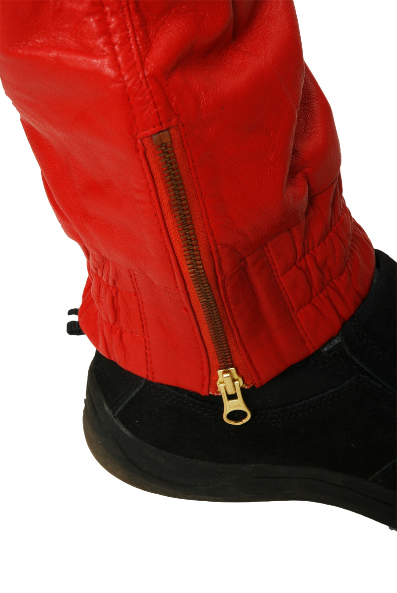 Close up picture of the ankle of red leather joggers, showing a wide elastic band and long gold zipper at the bottom