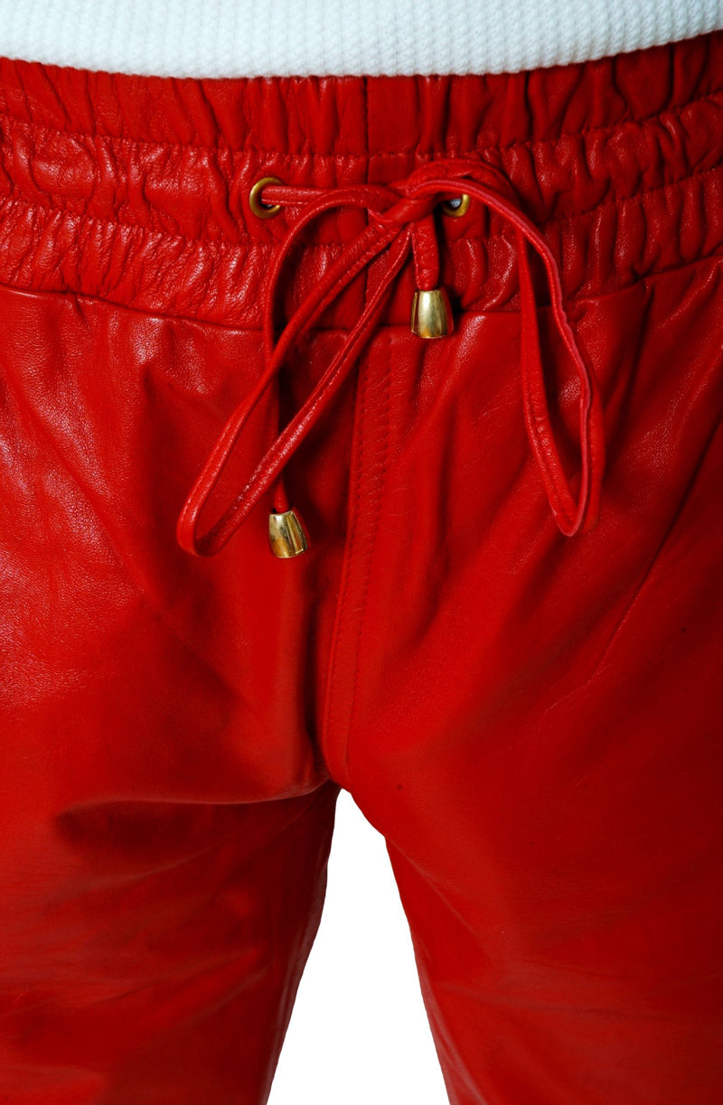 Close up picture of the waist of red leather joggers, showing the wide elastic waist and leather drawstring with metal tassels on ends.